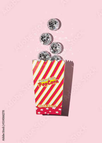 Popcorn box with shiny disco balls on pastel light pink background. Modern party concept. Creative food idea. Fun flavor inspiration.