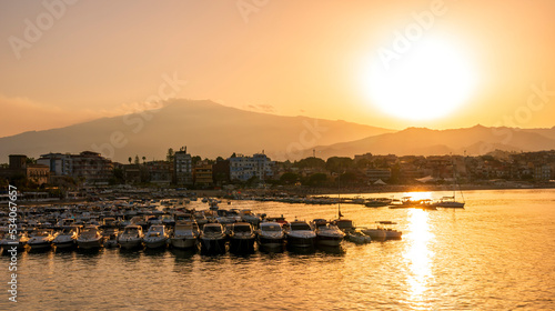 picturesque sunrise or sunset in a sea port with a gulf dock pier with tour boats and a town with cloudy sky on background of a seashore landscape