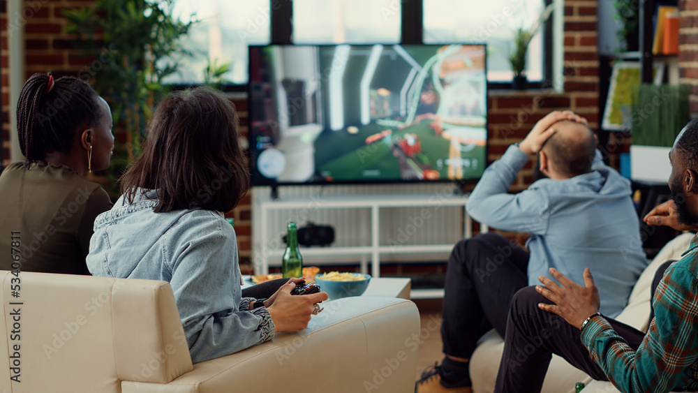 Diverse people playing video games to have fun at home, enjoying online shooting challenge on television console. Using controller to play competition at social gathering with friends.
