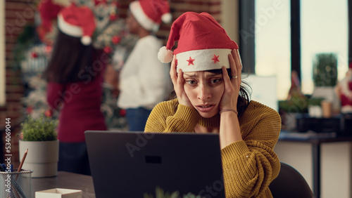 Frustrated tired woman trying to work in noisy office with christmas decorations and ornaments. Being interrupted by cheerful people celebrating xmas winter holiday at work, stressed person.