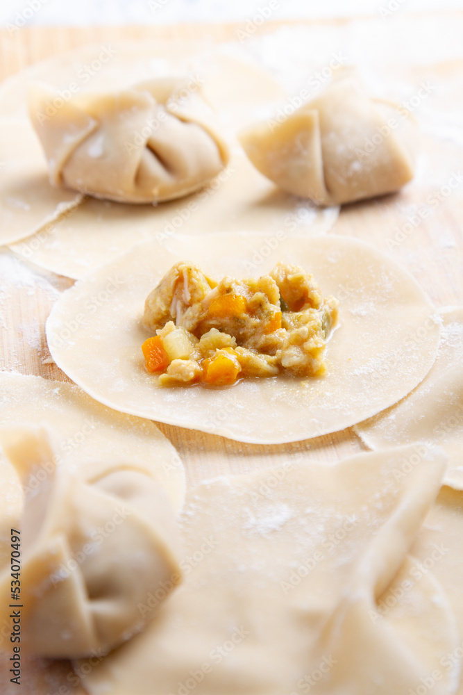 A wooden surface , showcasing dough pieces in the process of being crafted into dumplings. Several pieces are folded and sealed, while one remains open, revealing a vibrant vegetable filling A wooden surface , showcasing dough pieces in the process of being crafted into dumplings. Several pieces are folded and sealed, while one remains open, revealing a vibrant vegetable filling