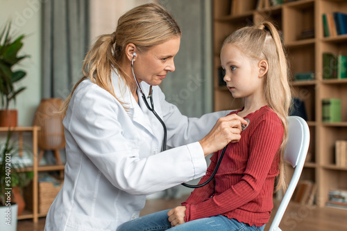Wallpaper Mural Female doctor checking child's lungs during medical checkup at home interior, using stethoscope to examine breathing Torontodigital.ca