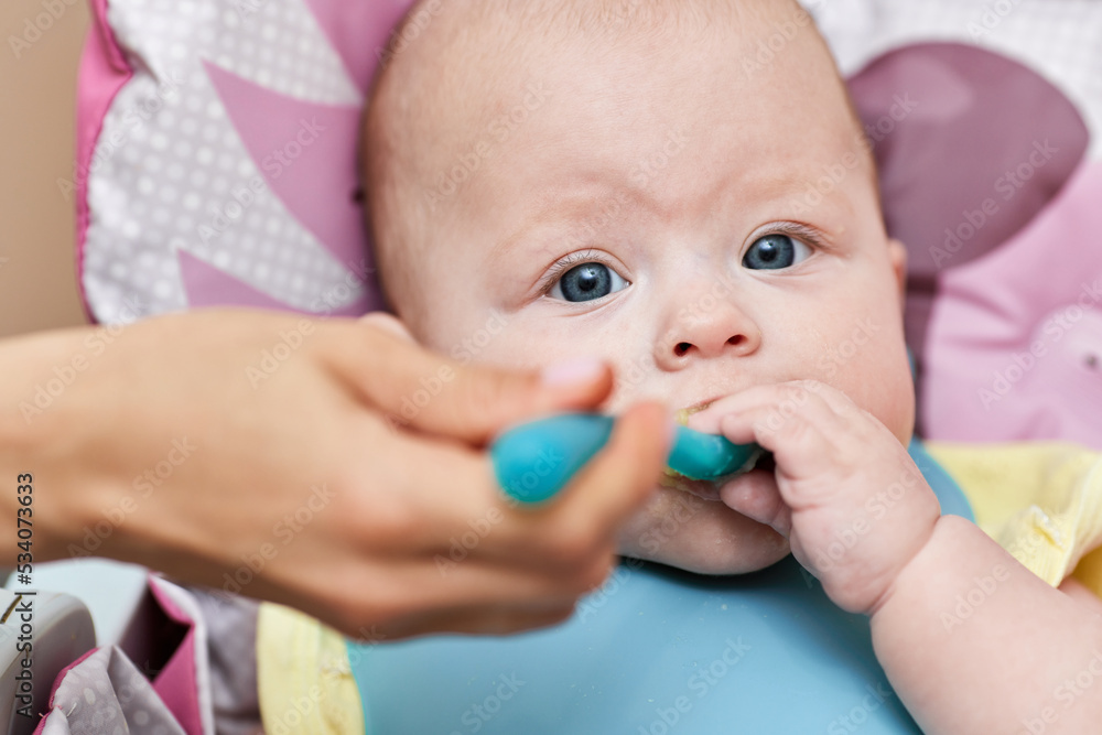Mom feeds her baby girl with a spoon on baby chair. Mom feeds her baby girl with a spoon on baby chair.