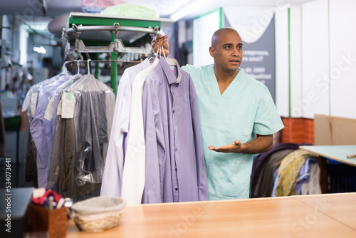 Portrait of dry cleaning employee at work, man giving clean clothes to client