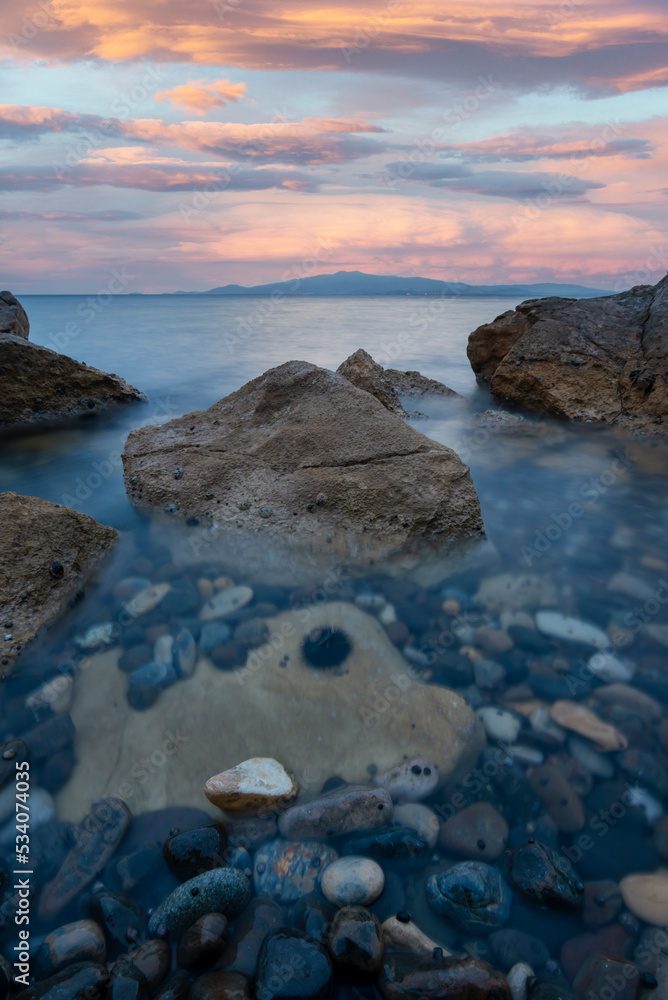 Long exposure photography, rocks on foreground and silky sea water and colorful clouds on background
