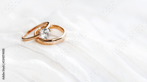 Pair of golden wedding rings on white textile background with copy space. Engagement ring with diamond on fabric backdrop. Symbol of love and marriage.