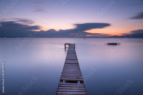 Long exposure photography, wodden pier on foreground and silky sea water and colorful clouds on horizon as a background