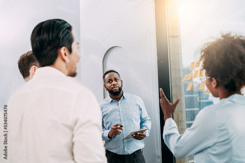 Obraz premium Groups of business people diverse brainstorming presentation ideas using label color sticky on glass wall together in the office, planning strategy new marketing projects, and teamwork concepts.