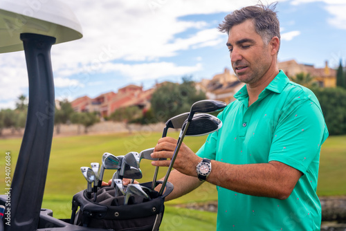 Man playing golf at golf club, checking golf clubs before hitting the ball