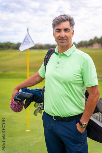 Portrait of male golfer walking down fairway carrying bags, playing golf