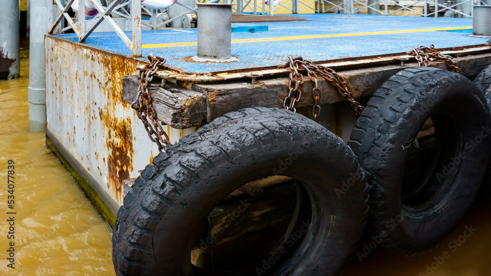 Fototapeta premium car tire with a metal chain on a old concrete sea pier,old truck tires at the pier.tire bumpers