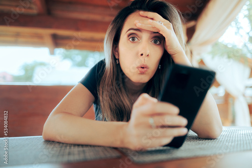 Surprised Girl Receiving a Strange Text Message. Woman waiting in a restaurant reading shocking news on her phone
