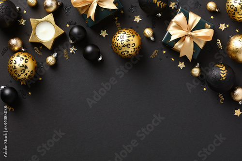 Stylish dark Christmas background with black and gold Xmas decorations, baubles, gift boxes, confetti. Flat lay, top view.