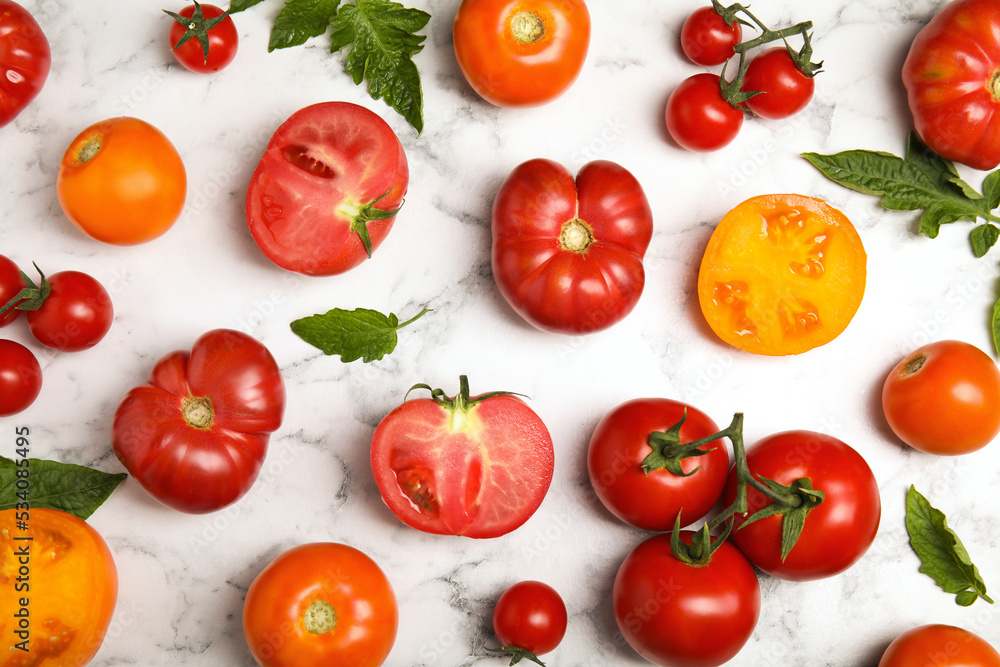 Flat lay composition with different ripe tomatoes and leaves on white marble table Flat lay composition with different ripe tomatoes and leaves on white marble table