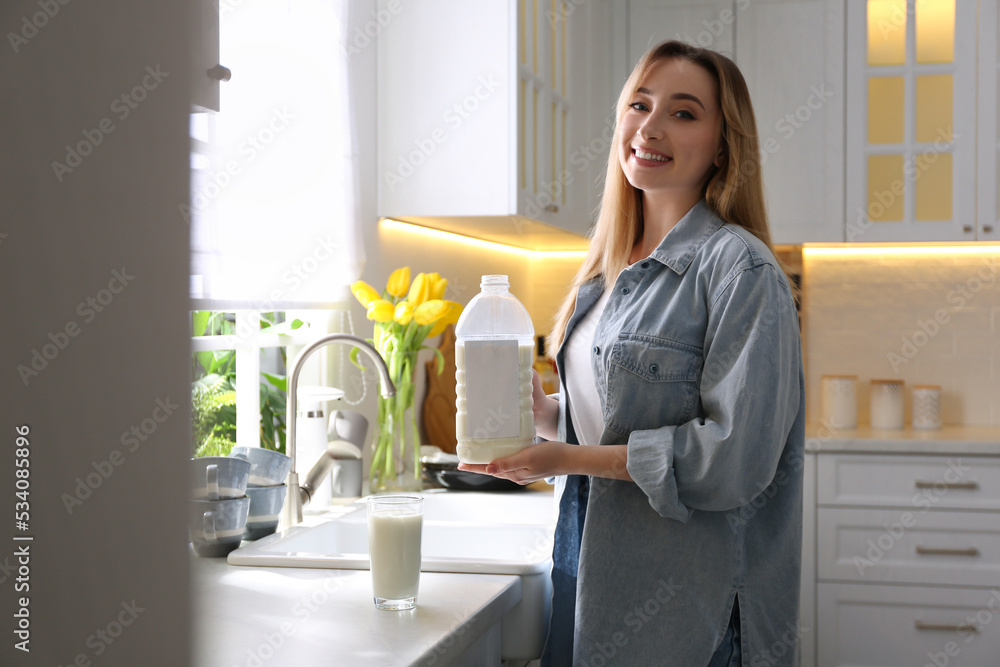 Young woman with gallon bottle of milk and glass at white countertop in kitchen Young woman with gallon bottle of milk and glass at white countertop in kitchen