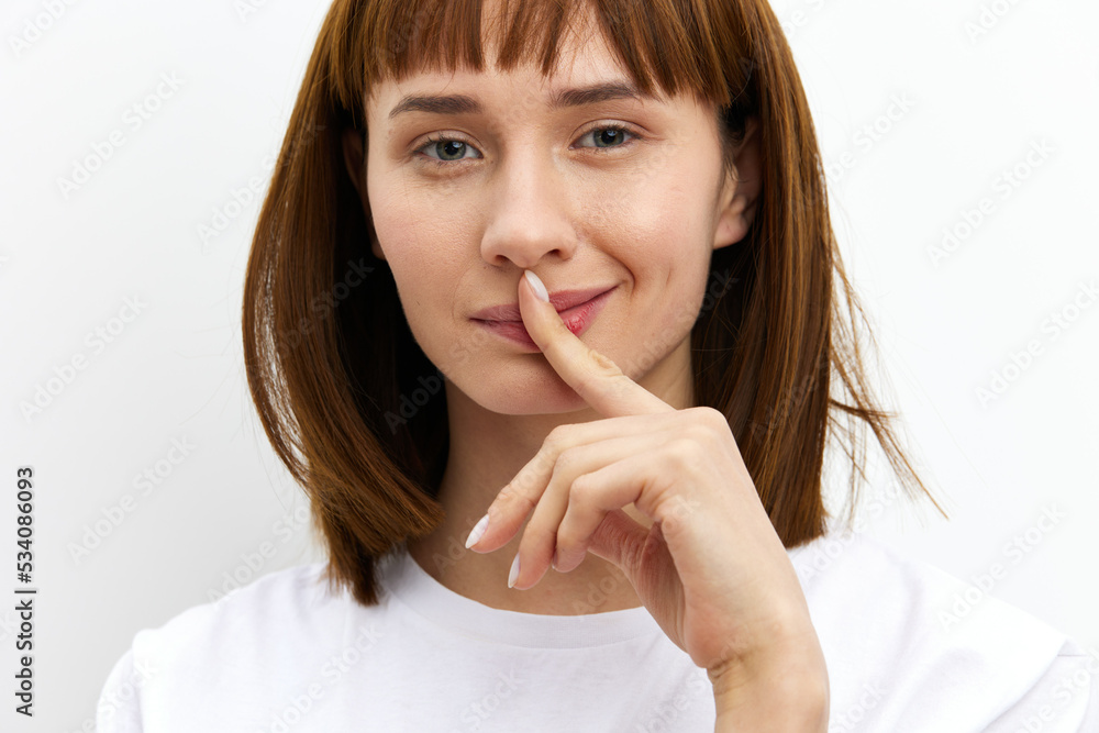 a close horizontal photo of a funny, thoughtful woman in a white T-shirt on a white background holding a finger near her face in reflection a close horizontal photo of a funny, thoughtful woman in a white T-shirt on a white background holding a finger near her face in reflection