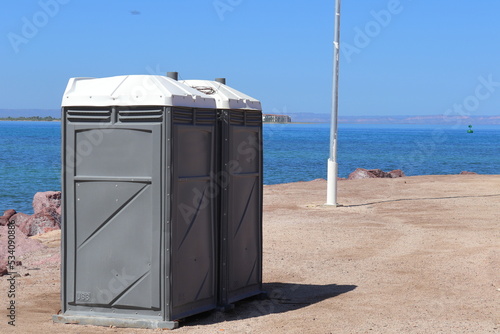 Two public restrooms in gray color on a beach. In the background, the pacific ocean