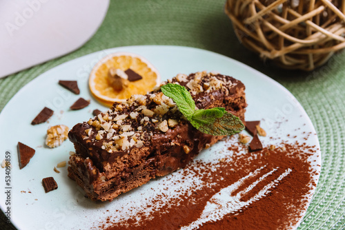 Sweet breakfast with chocolate honey biscuit cake with sour and butter cream and walnuts, a slice of dried orange and decorated with mint leaf and cocoa powder