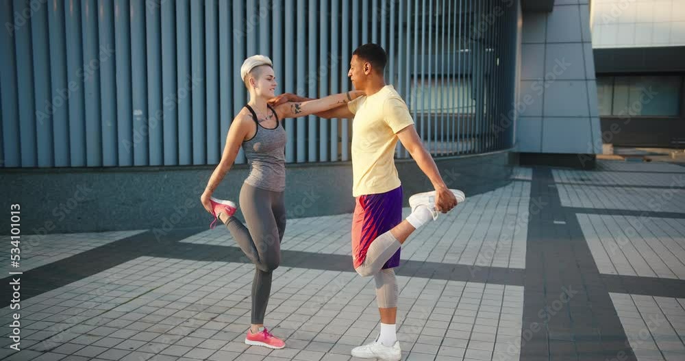 Multinational fit couple leans on each other warming up legs Multinational fit couple leans on each other warming up legs
