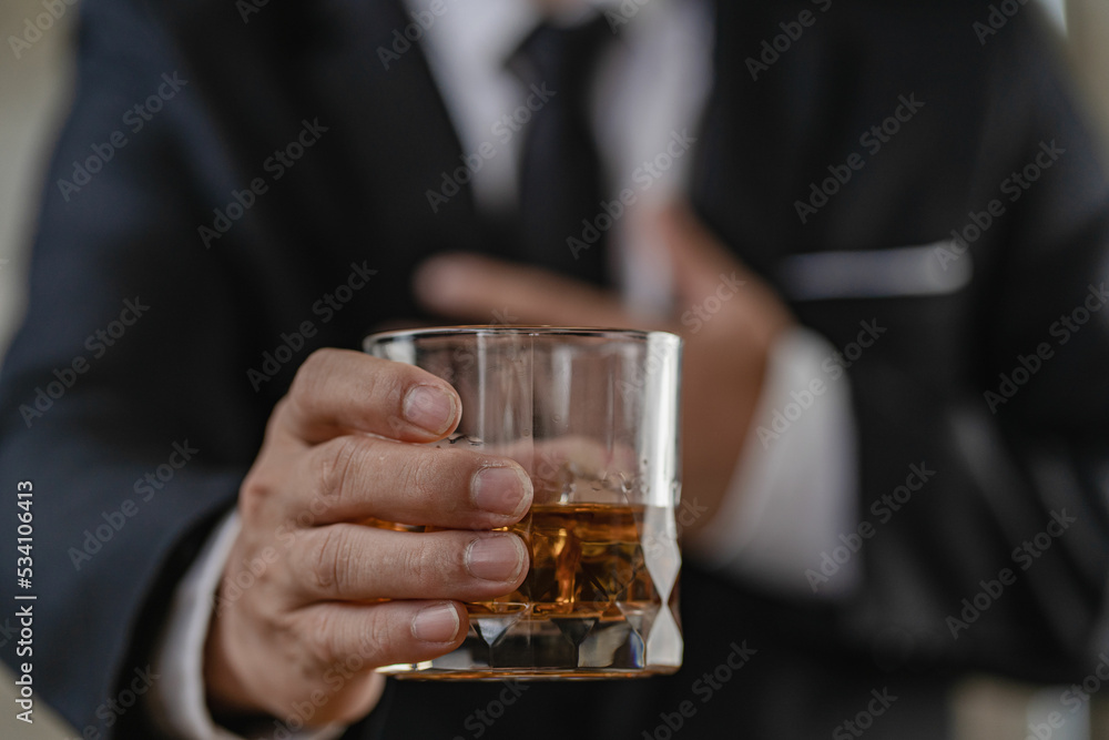 The bartender holds a glass of whiskey and ice to the male guest. The rest of the concept in the bar Close-up of serious businessman holding whiskey showing executive privilege concept.