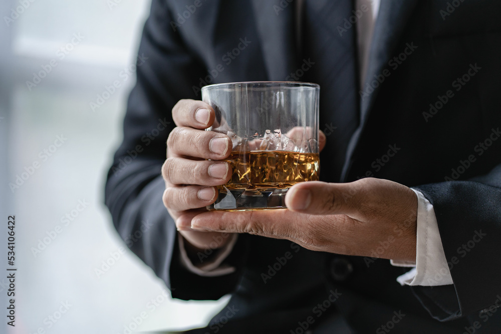 The bartender holds a glass of whiskey and ice to the male guest. The rest of the concept in the bar Close-up of serious businessman holding whiskey showing executive privilege concept. The bartender holds a glass of whiskey and ice to the male guest. The rest of the concept in the bar Close-up of serious businessman holding whiskey showing executive privilege concept.