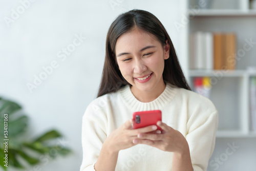 Beautiful young Asian woman smiling enjoying social media on mobile phone.