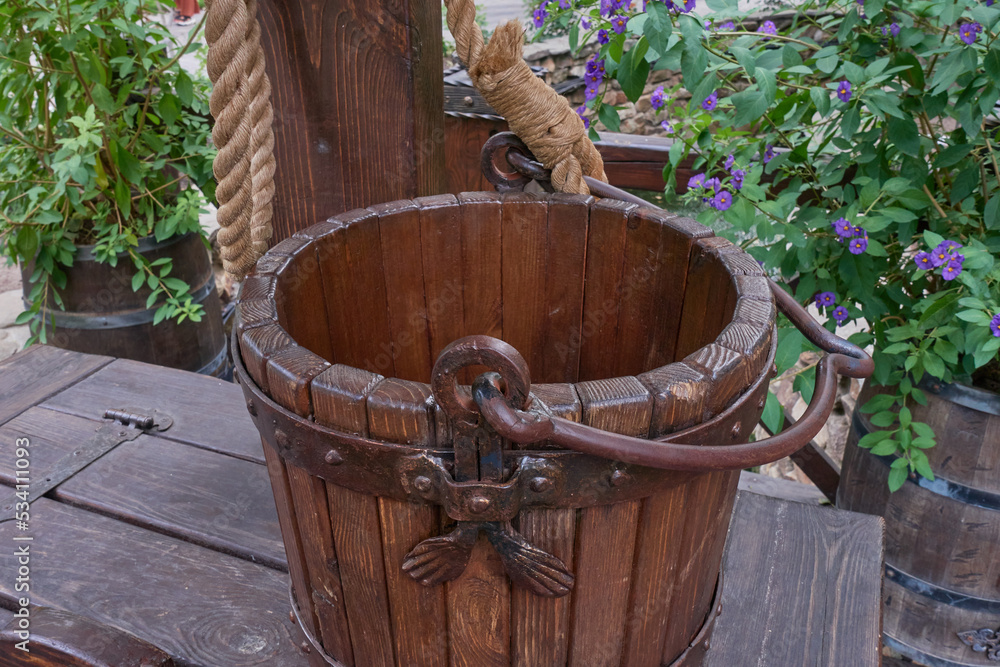Wooden bucket on a rope. A bucket in a wrought iron frame stands on top of a well in the garden. Selective focus.