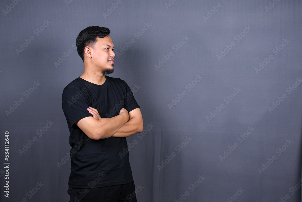 Smiling handsome asian man in black t-shirt standing with crossed arms isolated on gray background