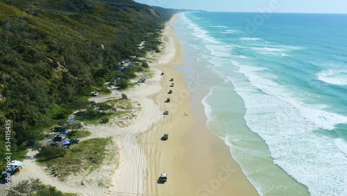 4K Aerial Drone Over 4WD Cars Driving On Sandy Beach With Blue Ocean Waves Lapping Shore In Australia photo