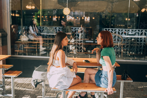 Two pretty girlfriends talking while sitting in a bar outdoors