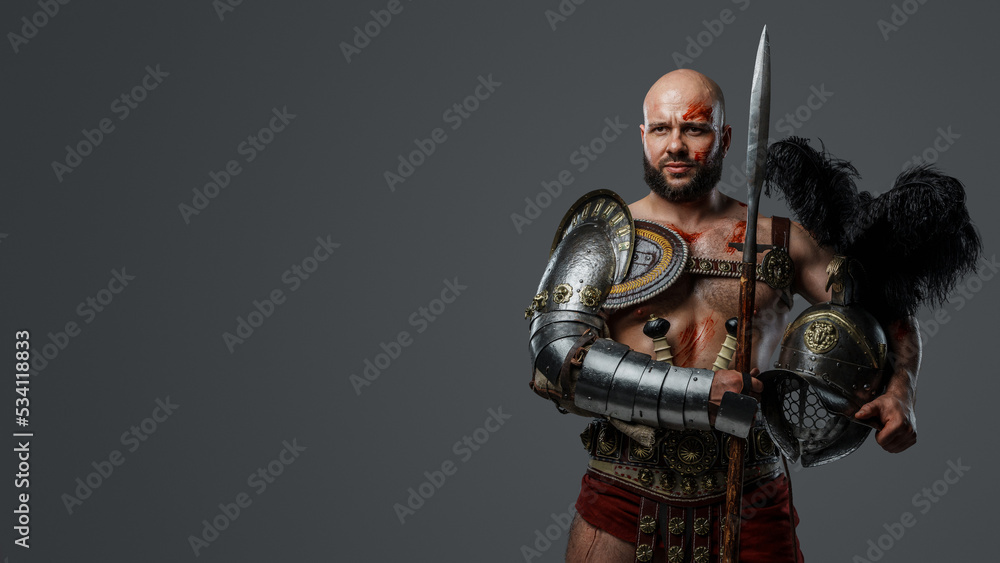 Naklejka premium Portrait of handsome gladiator with muscular build holding long spear and plumed helmet.