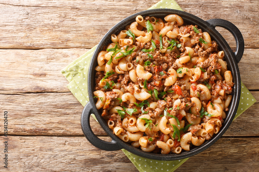 Homemade Hamburger Macaroni and Cheese with Parsley closeup in the pan on the wooden table. Horizontal top view from above