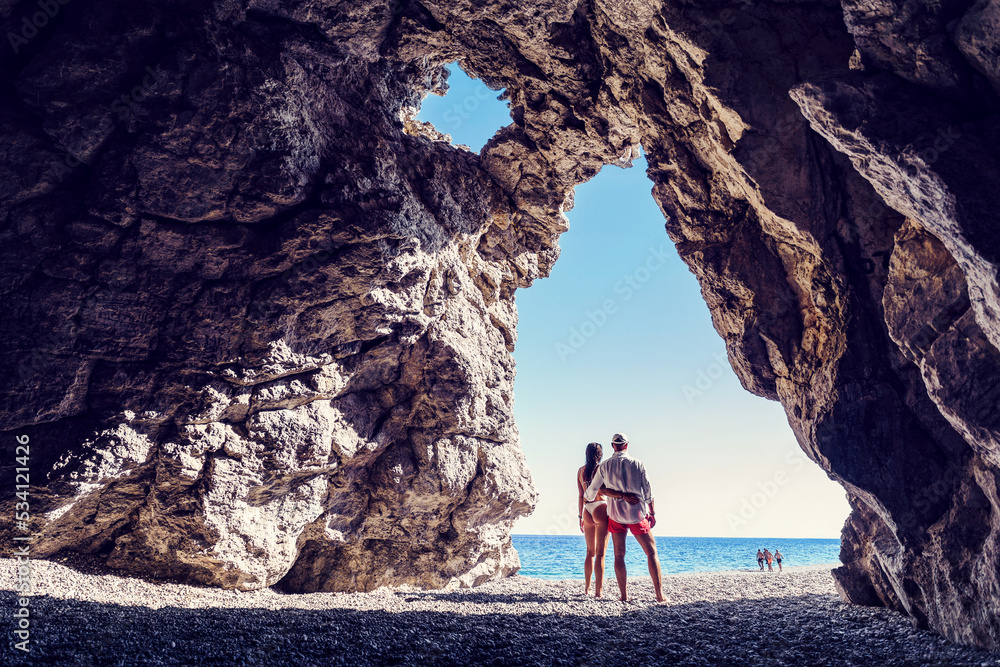 Kobieta i mężczyzna przytuleni w jaskini z widokiem na morze - obrazy, fototapety, plakaty 
