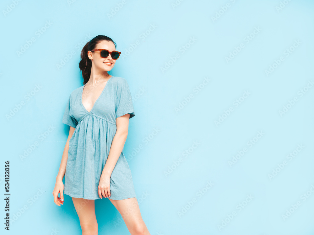 Young beautiful smiling female in trendy summer dress. carefree woman posing near blue wall in studio. Positive brunette model having fun.Cheerful and happy. Isolated Young beautiful smiling female in trendy summer dress. carefree woman posing near blue wall in studio. Positive brunette model having fun.Cheerful and happy. Isolated