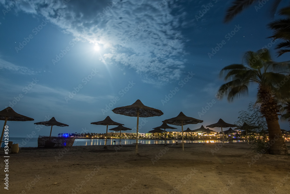 sandy beach with beach umbrellas and a bright moon in the night