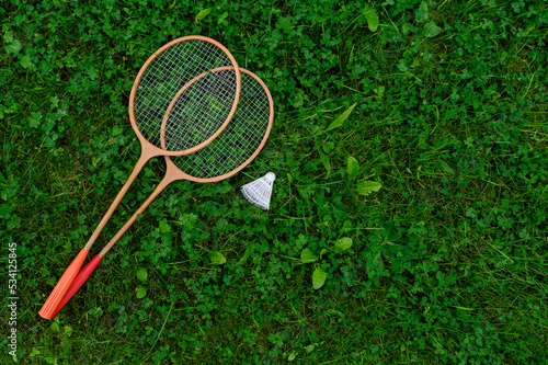 Badminton rackets and a shuttlecock lie on a green lawn. The concept of active recreation, outdoor games.Top view