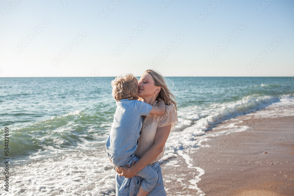 Mom and son are walking on the beacj, the woman hugs and kisses the child in her arms. people together. Mom and son are walking on the beacj, the woman hugs and kisses the child in her arms. people together.
