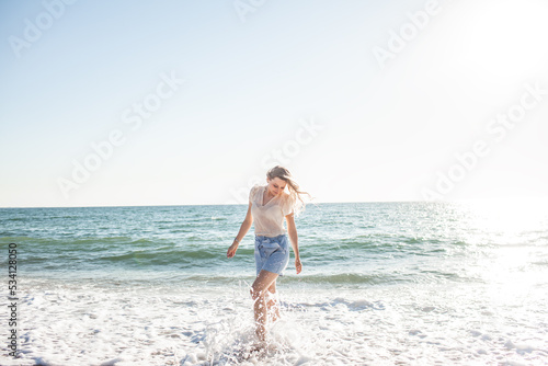 A beautiful girl dressed in a blue shorts and a white light blouse runs on a deserted beach, enjoys freedom and loneliness and look at the biew of the ocean