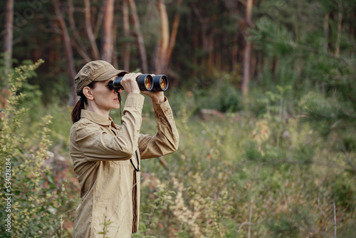 Tableau sur toile A woman park ranger in uniform looks through binoculars and monitoring the forest area in summer, selective focus