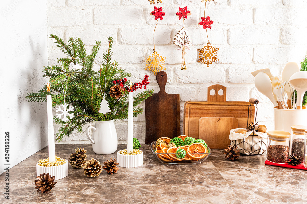 a fragment of a part of a modern kitchen with various Christmas decorations, candles, a plate of dried orange slices. marble table. brick wall.