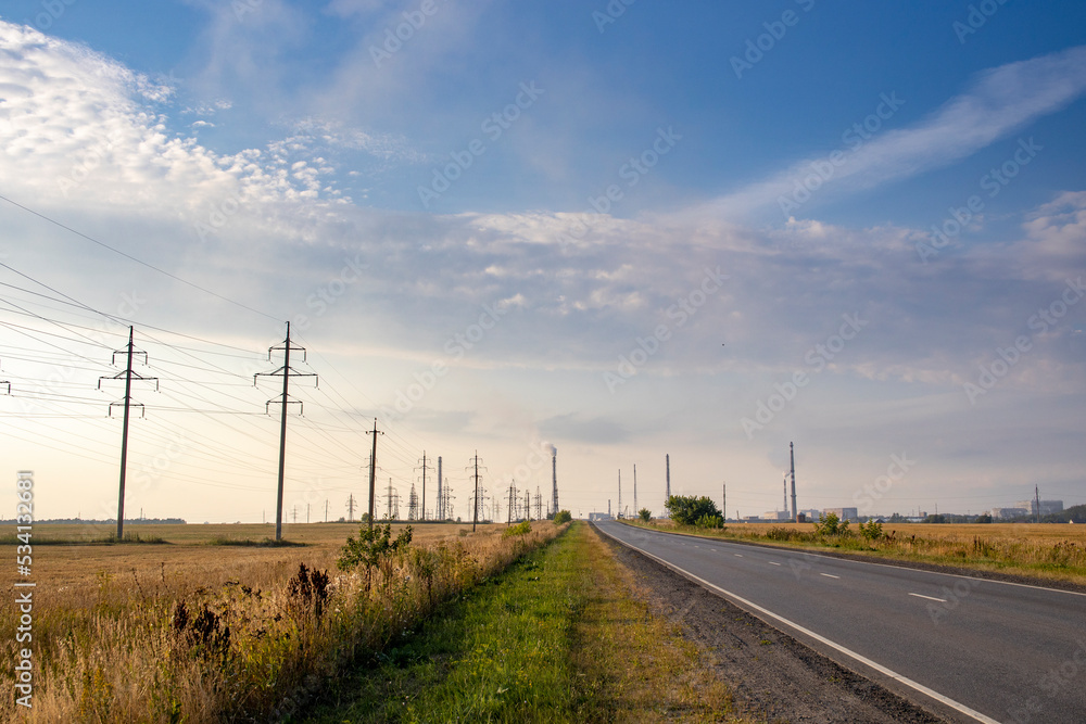 Power lines along the road. Asphalt road and high voltage power towers. Power lines along the road. Asphalt road and high voltage power towers.