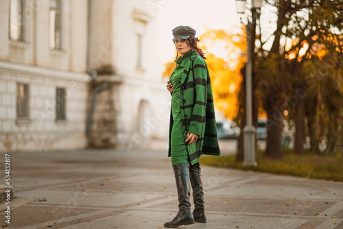 Outdoor fashion portrait of an elegant fashionable brunette woman, model in a stylish cap, green dress, posing at sunset in a European city in autumn. © svetograph