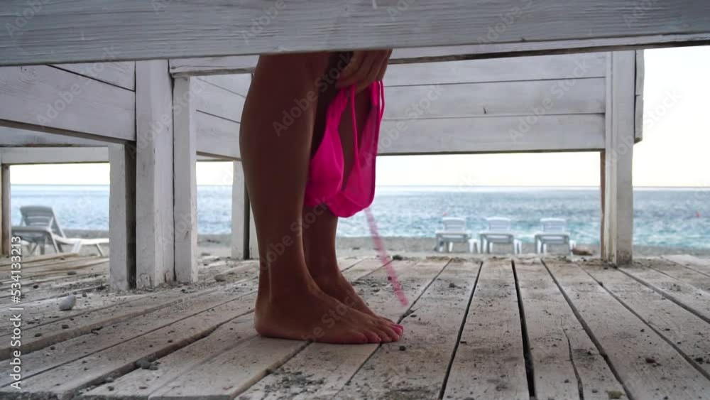 Woman in the changing, dressing room on the beach, at sunset on the  seashore. The girl changes clothes, throwing up a swimsuit, then leaves the  locker room in a pink dress. Close up, slow motion