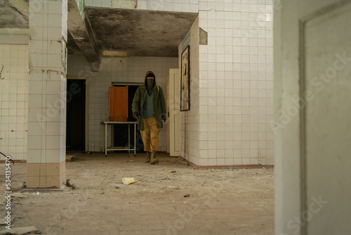 Young man walking in an abandoned building. wandering guy. man in a protective cloak with a hood. Post apocalypse. Traveling in a post-apocalyptic world.