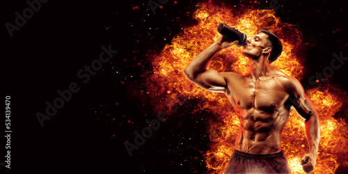 Muscular man with protein drink in shaker over dark background with fire flames