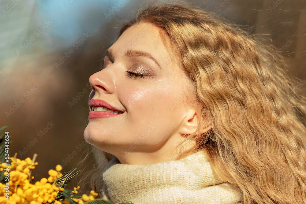 Naklejka premium Portrait of a young woman with blond hair holding a bouquet of mimosa in her hands. Spring