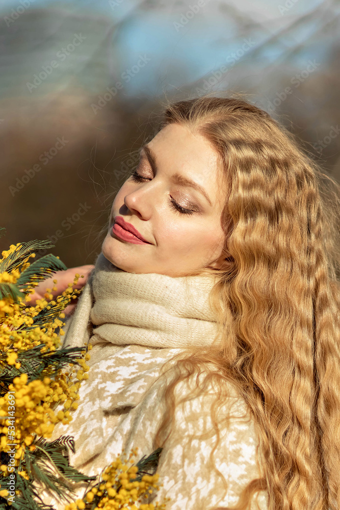 Portrait of a young woman with blond hair holding a bouquet of mimosa in her hands. Spring Portrait of a young woman with blond hair holding a bouquet of mimosa in her hands. Spring