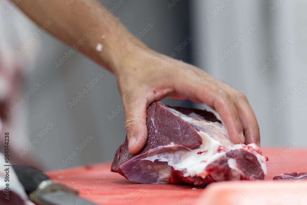 A butcher cuts fresh beef into pieces, using a sharp knife. Blurred background