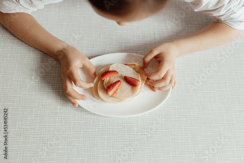 Hungry little girl eat sweet panckaces with strawberries. Family breakfast concept photo