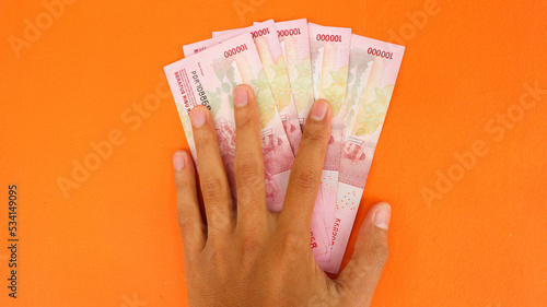 Hand holding banknotes with a total of five hundred thousand rupiah isolated on orange background. Indonesian rupiah currency photo